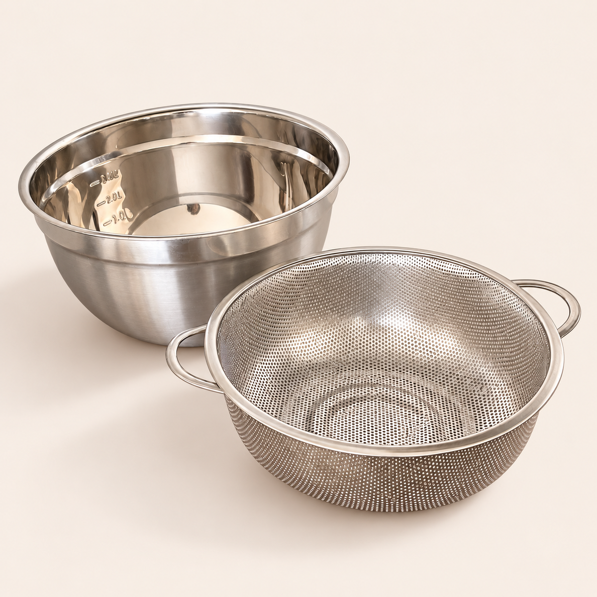24cm stainless steel strainer with two handles next to its mixing bowl with measuring marks